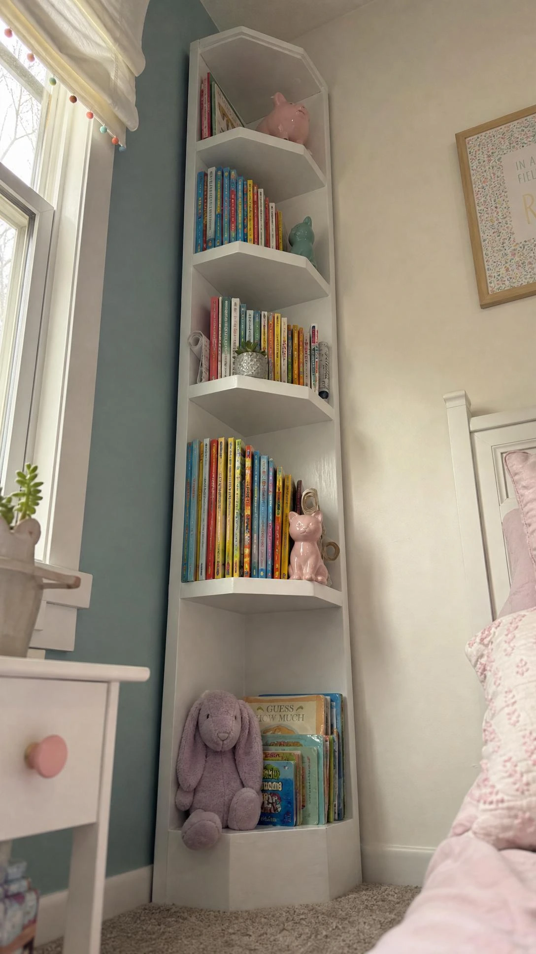 Tall narrow white corner tower bookcase rising dramatically toward the ceiling in a small child's bedroom, maximizing vertical storage space in an unused corner