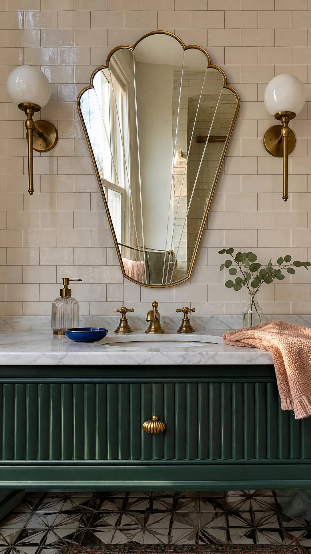 Tall scalloped Art Deco bathroom mirror with brass trim over an emerald fluted vanity, reflecting daylight and cream tile