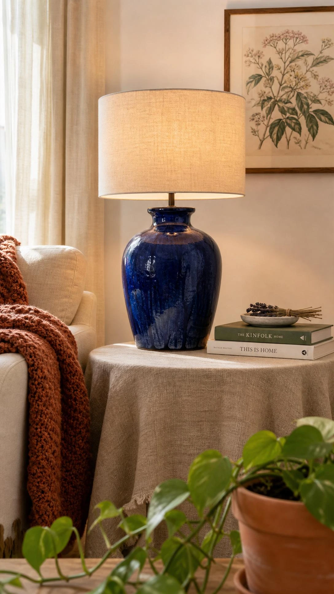 Cobalt blue ceramic table lamp with hand-thrown glaze texture and cream linen shade glowing on a natural side table in a warm living room corner