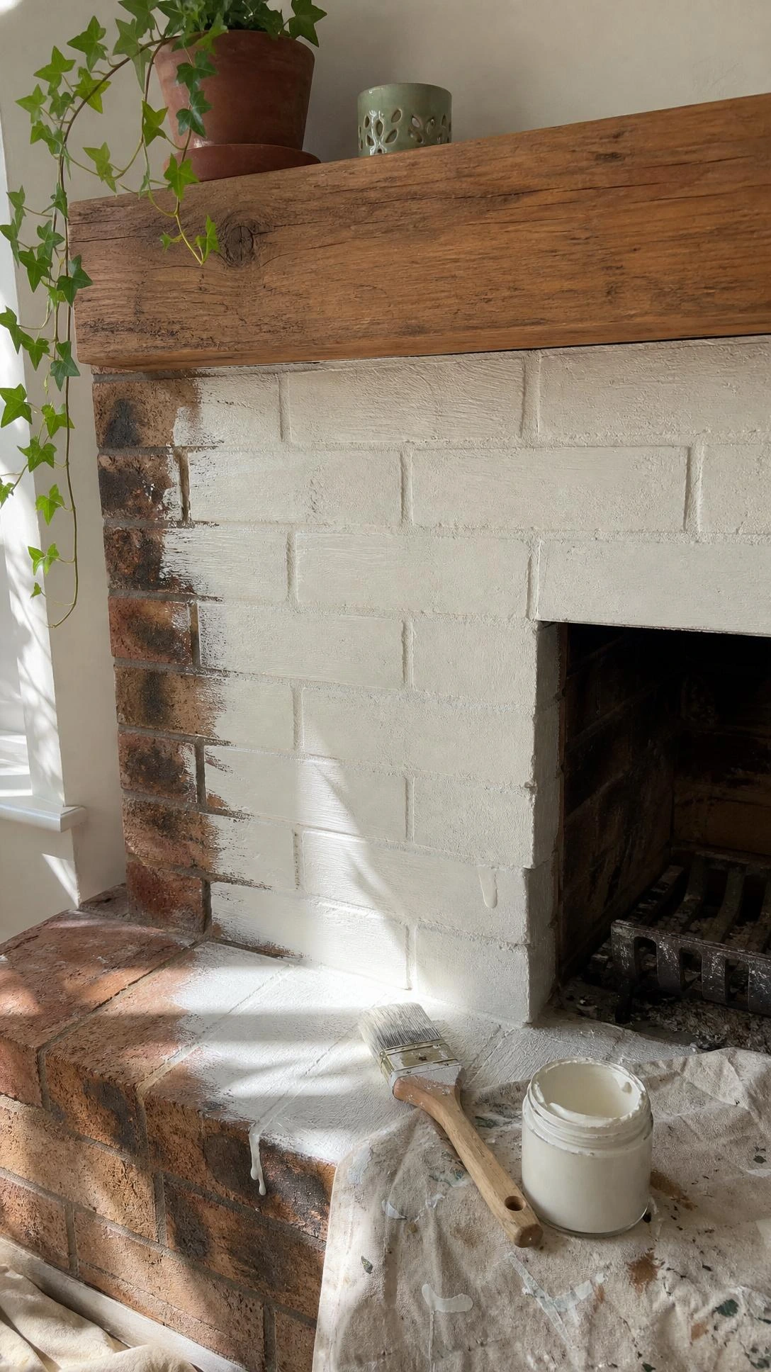 Brick fireplace surround mid-transformation with chalk paint, showing sharp contrast between stained rust-brown original brick and fresh matte white coverage