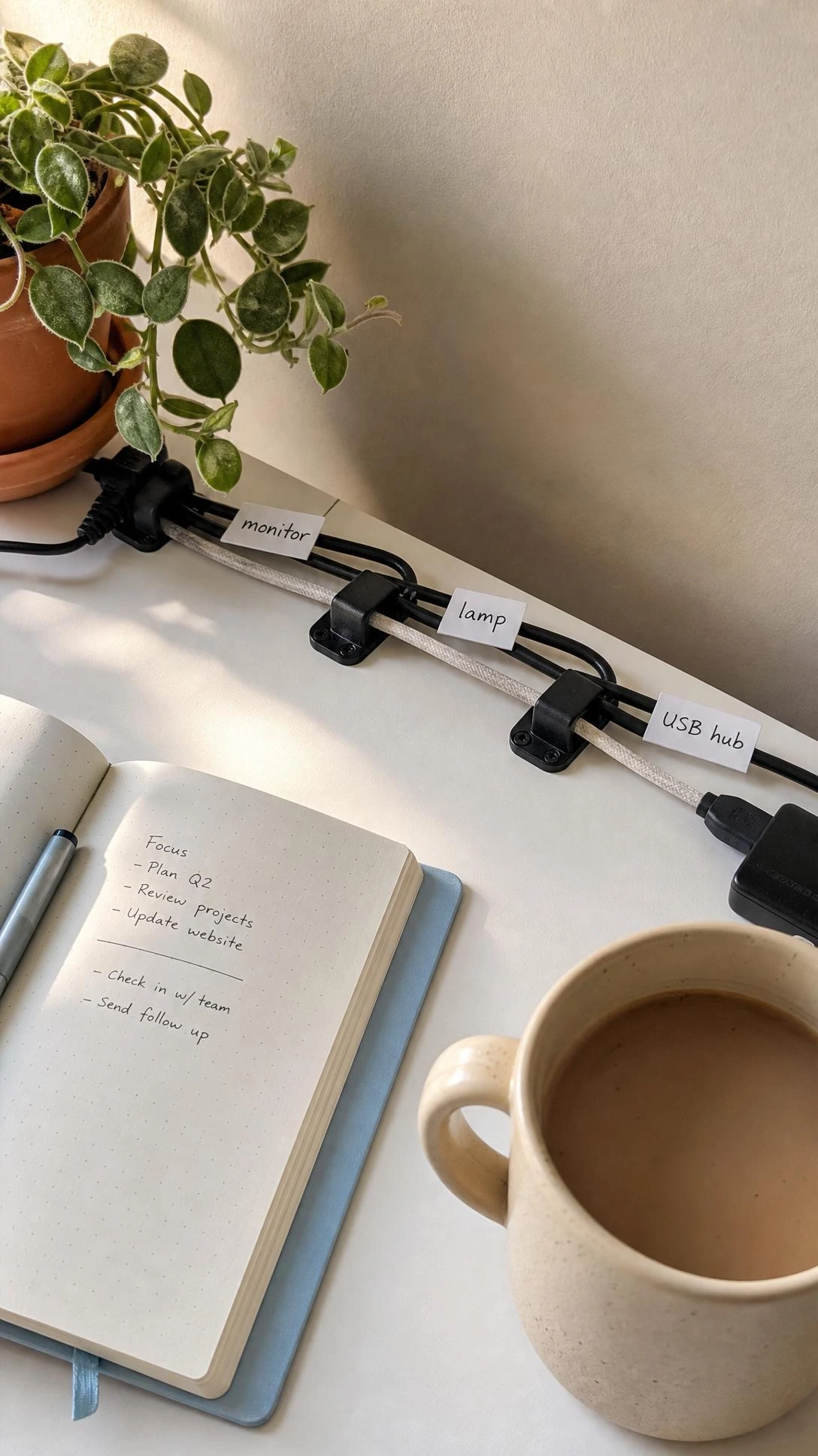 Neatly labeled USB and power cables clipped along the back edge of a white desk, showing how cord labels eliminate the tangle guessing game in a home office setup
