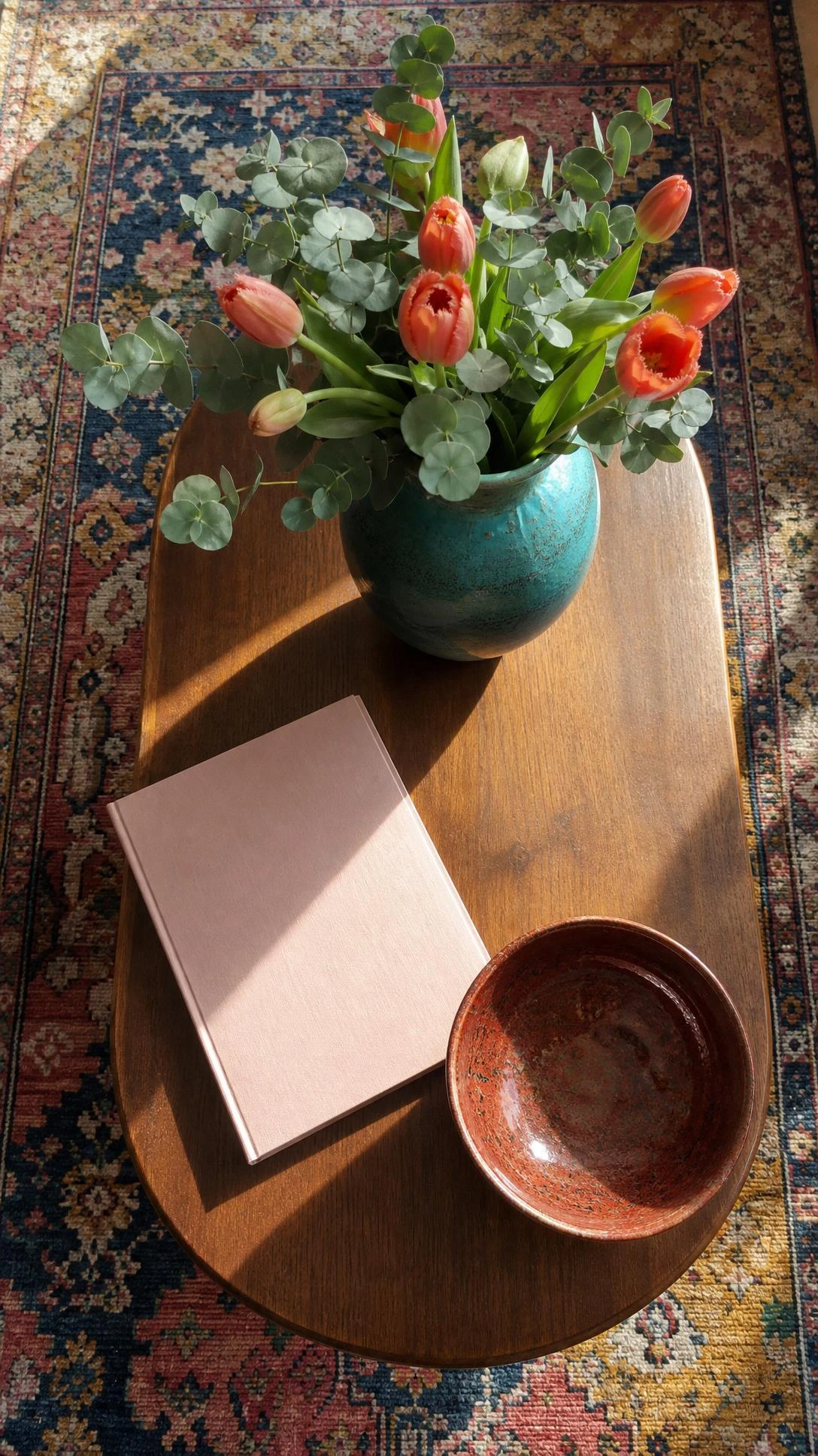 Overhead coffee table with a teal vase of eucalyptus and tulips plus a rust bowl, showing tiny home decor ideas with fewer larger accents
