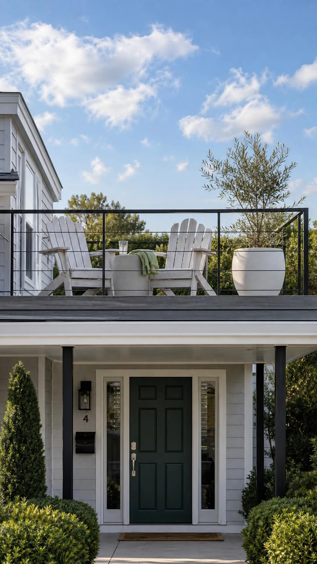 Modern home exterior with flat porch roof converted to rooftop deck, featuring grey composite decking and black metal railing above the front entryway