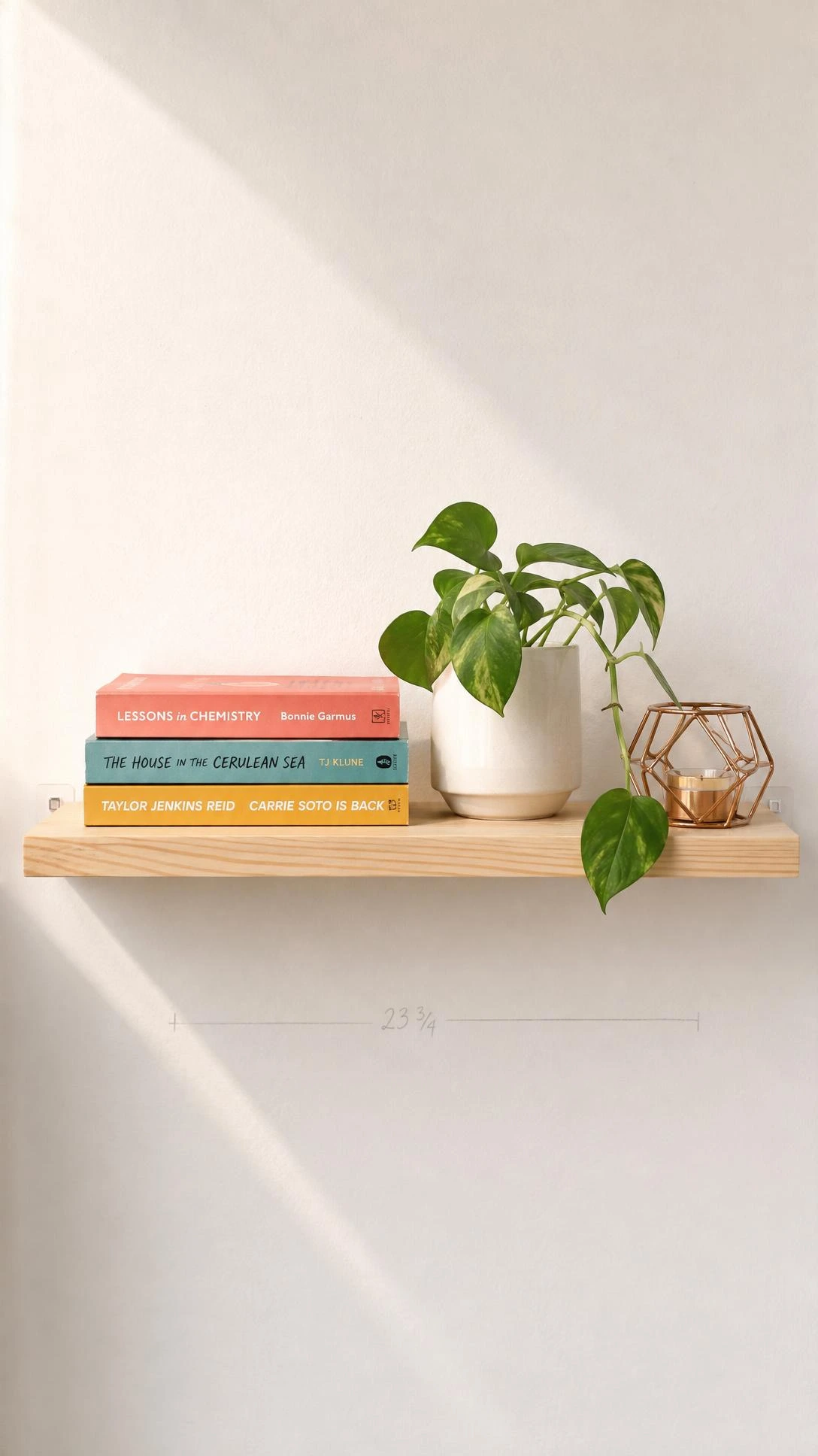 Light pine floating shelf mounted with removable adhesive strips, styled with coral, teal, and mustard paperbacks and a trailing pothos — dorm room wall decor that leaves no damage behind
