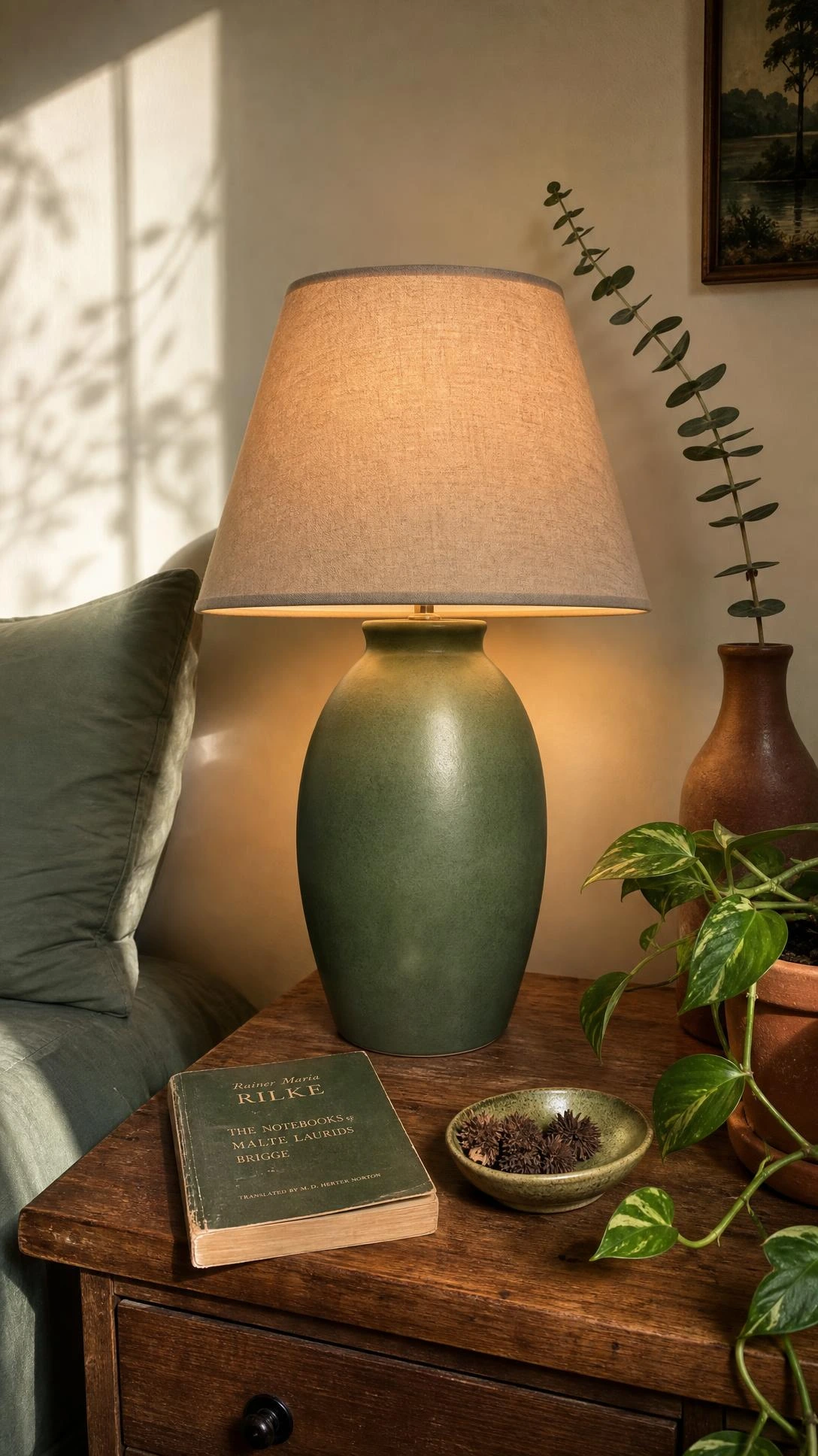 Jade green ceramic table lamp with matte glaze on a wooden nightstand casting warm amber light in a cozy bedroom corner