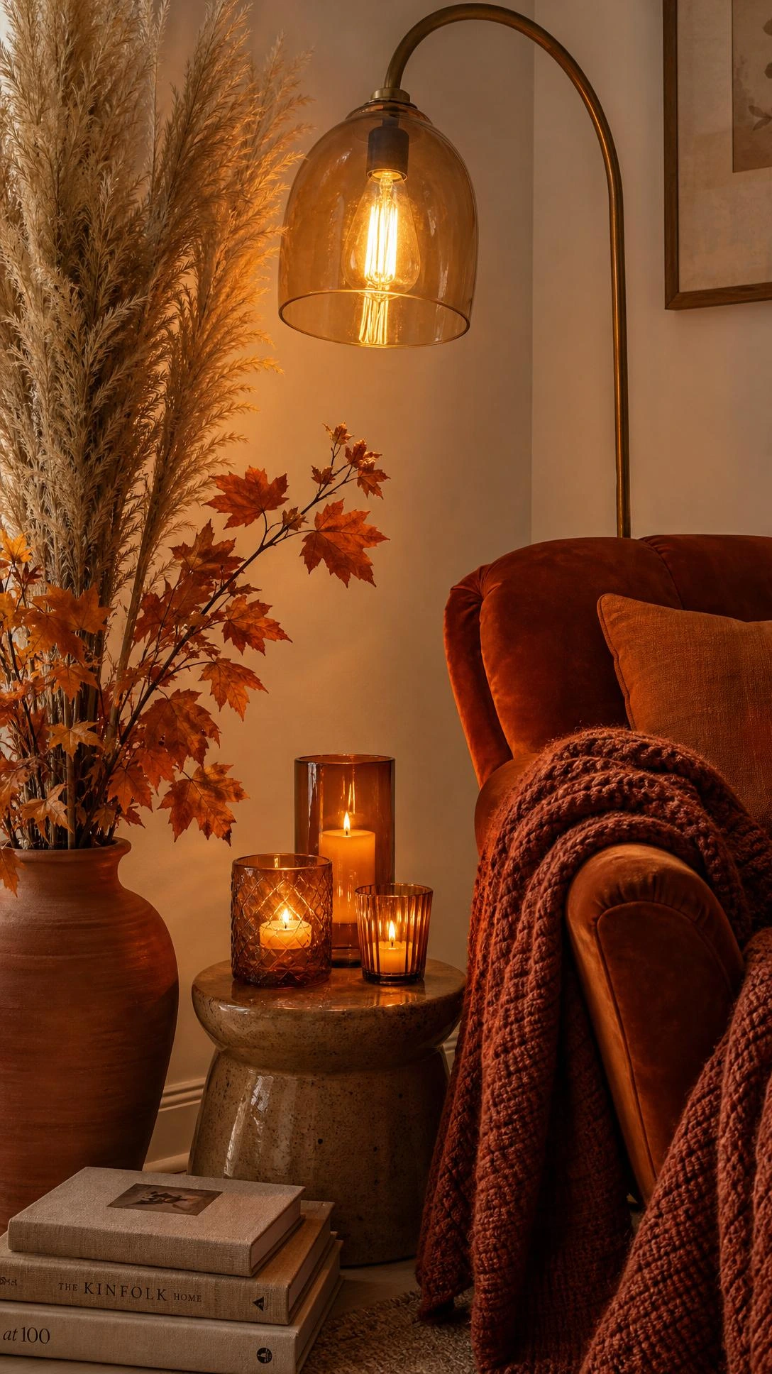 Tall arc floor lamp with amber Edison bulb casting warm honeyed light over a rust-orange velvet armchair layered with chunky knit throw for cozy fall living room ambiance