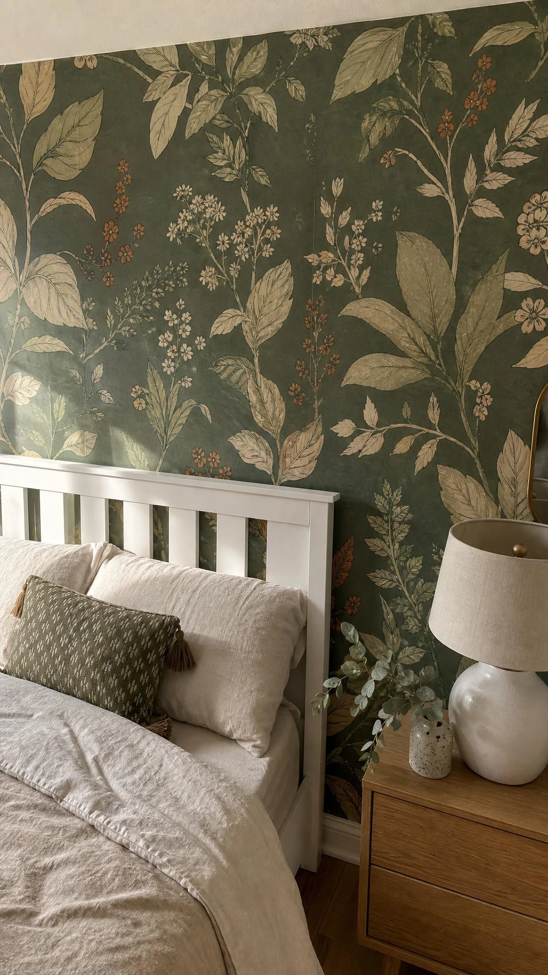 Bedroom corner with peel-and-stick wallpaper accent wall featuring moody sage green botanical print in olive, ivory, and terracotta tones