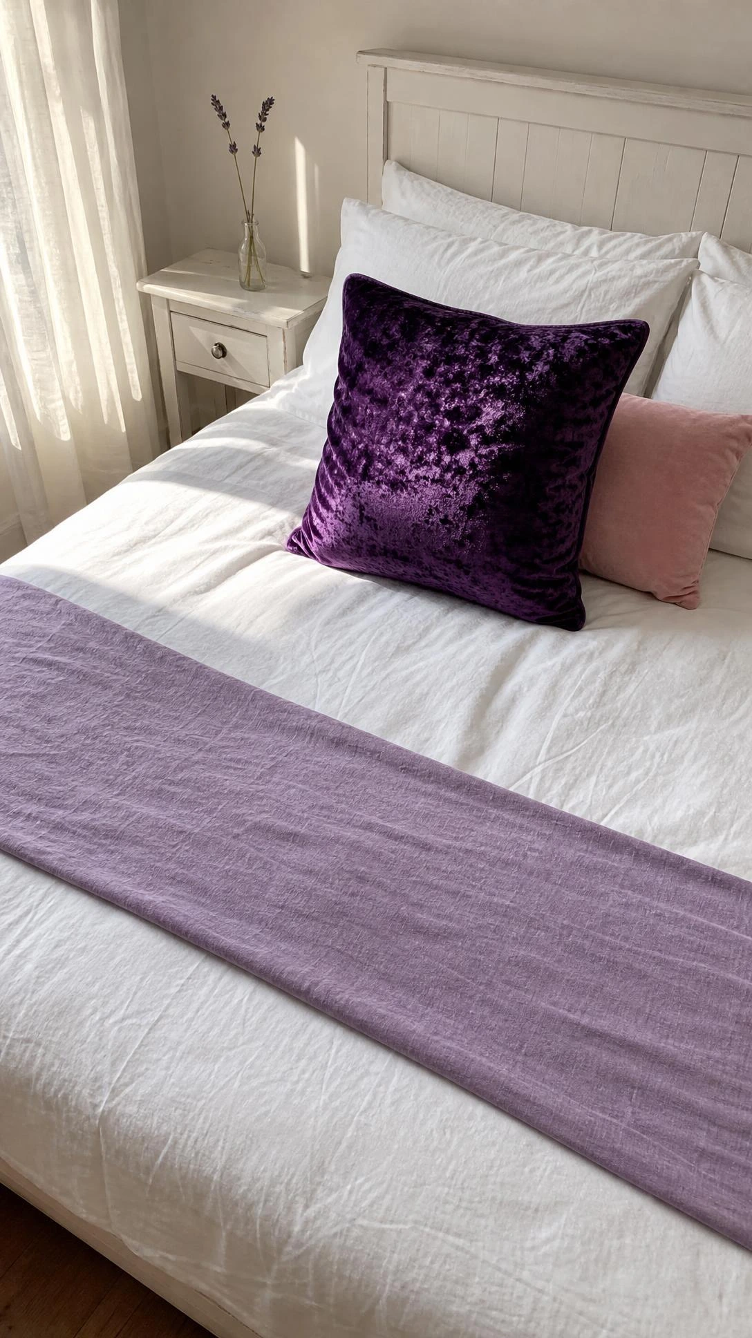 Deep purple crushed velvet accent pillow centered on a crisp white bed, warm natural light highlighting the rich fabric texture in a girls bedroom