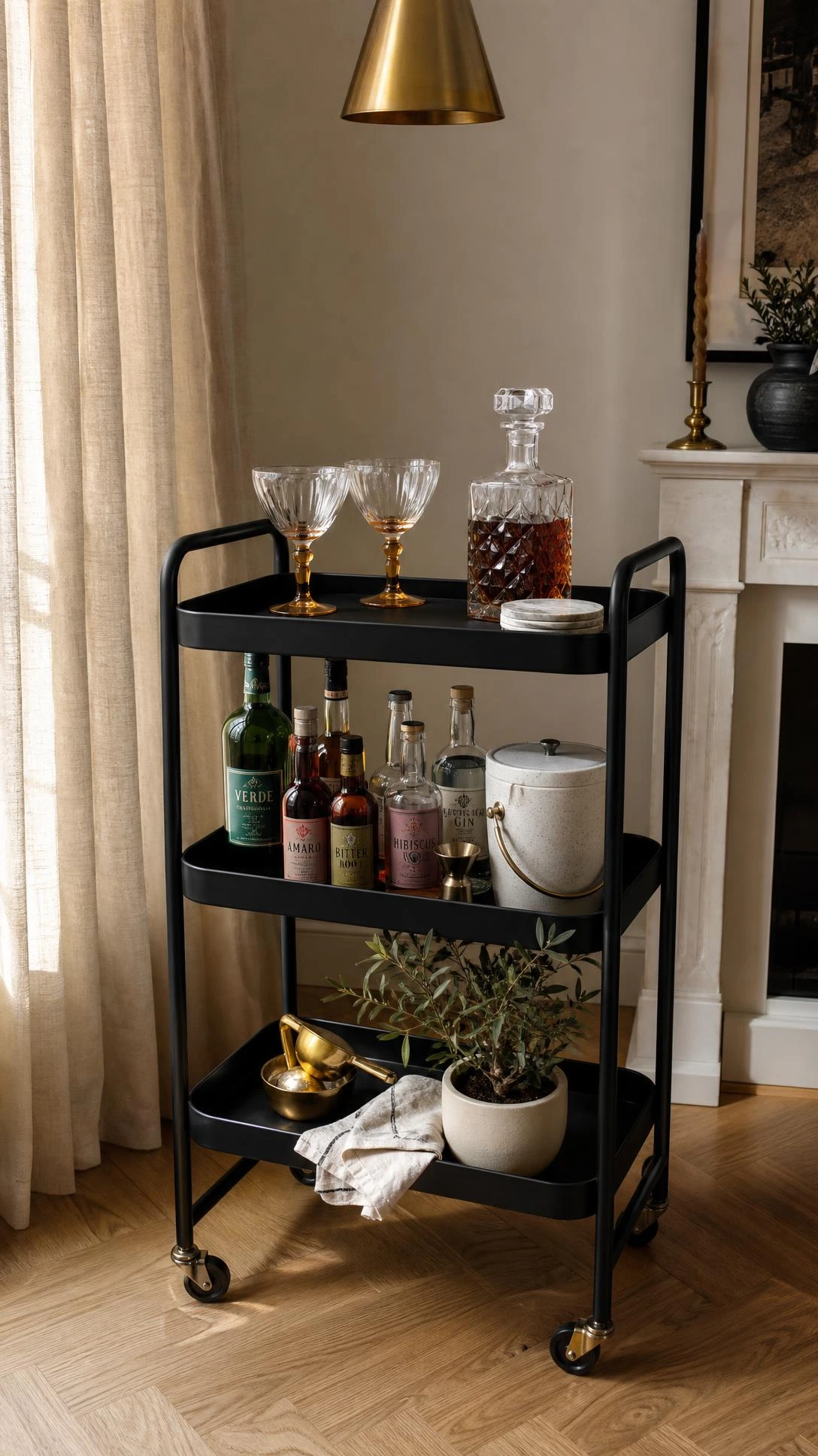 IKEA RASKOG cart painted matte black and styled as a bar cart with crystal decanter, cocktail glasses, and copper bar tools in a sunlit living room corner