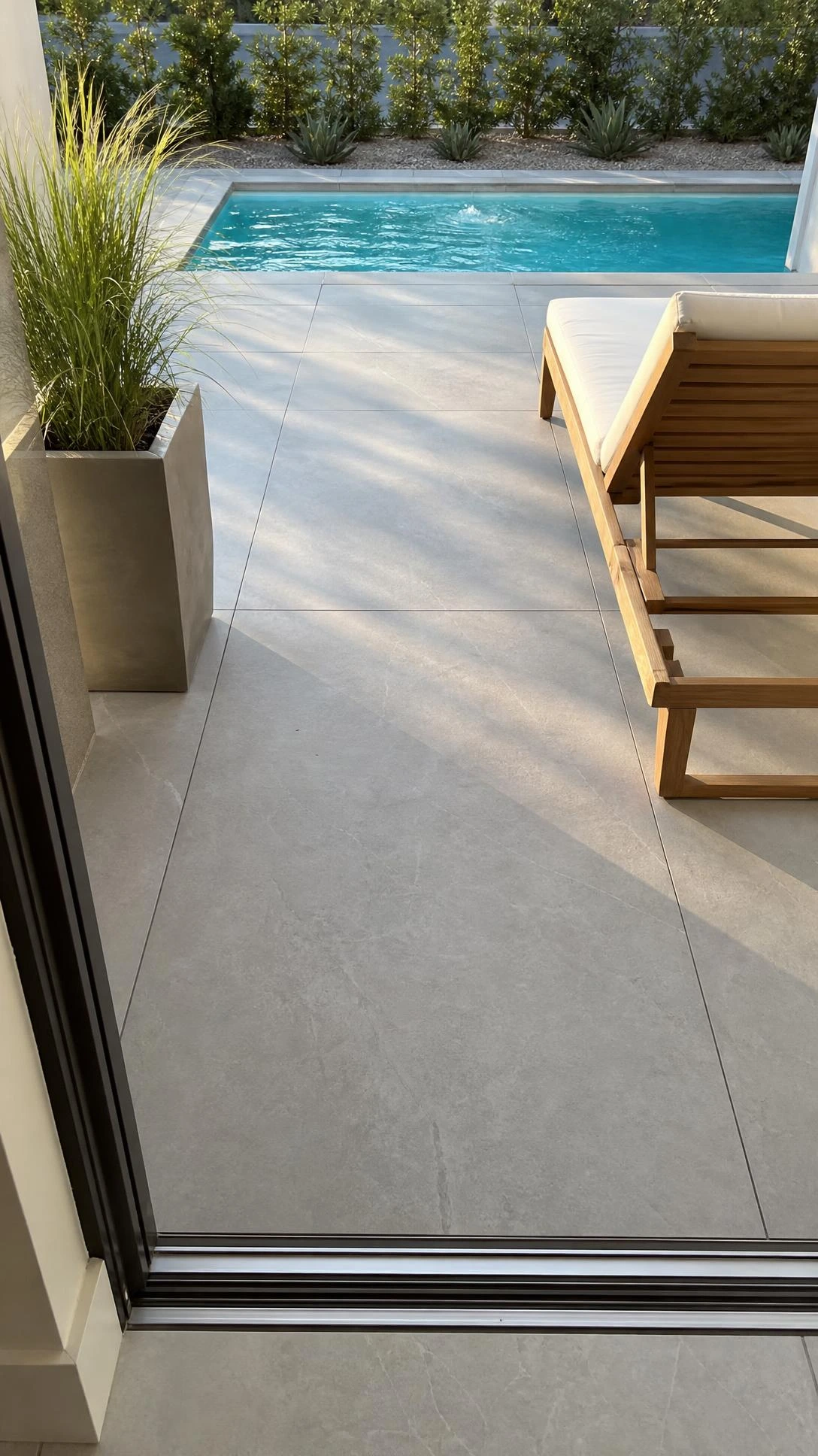 Continuous large-format light grey porcelain pavers stretching unbroken from house wall to pool waterline, showing how a single surface backyard patio design visually expands a compact space