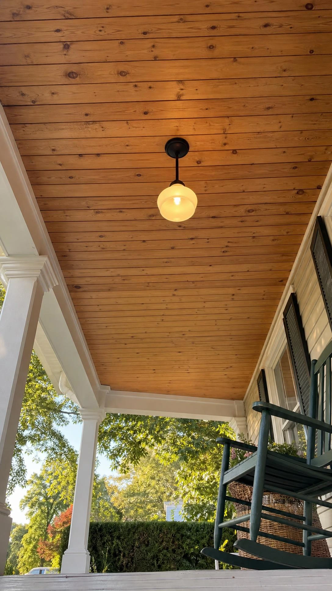 Low-angle view of a tongue and groove porch ceiling with warm honey-toned pine boards running in long parallel lines, showing natural wood grain and knots overhead