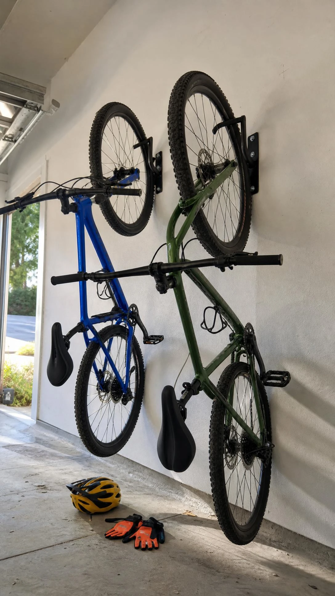 Two bicycles hanging on black metal wall-mounted bike hooks in a clean white garage — a cobalt blue and forest green bike stored vertically to free up floor space