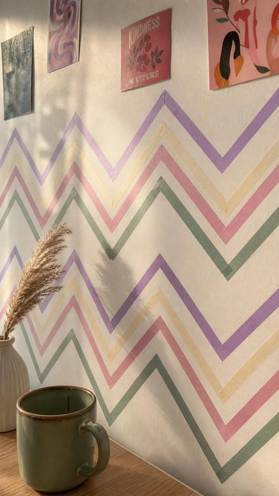 Dorm room wall decorated with washi tape in lavender, dusty rose, sage green, and cream arranged in a precise geometric chevron border pattern against white paint