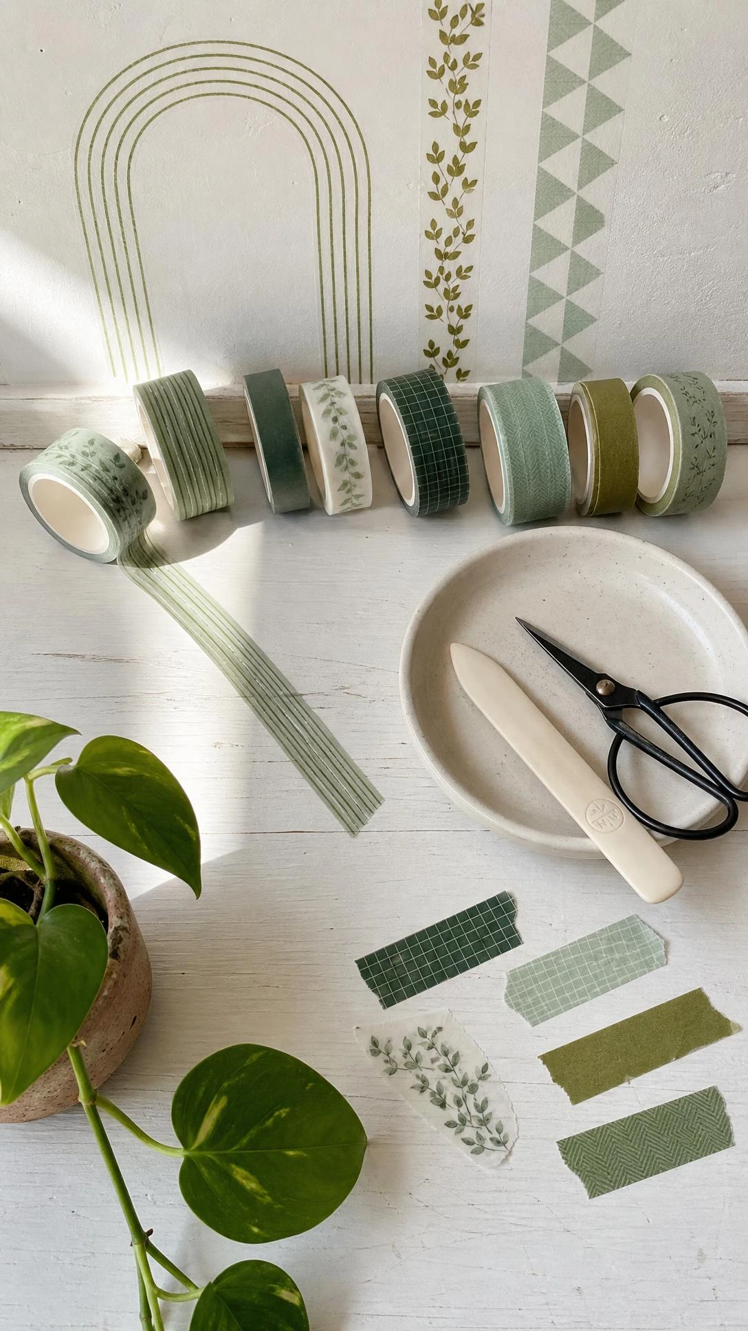 Overhead flat lay of washi tape rolls in sage, forest, mint, and olive green tones arranged on a white wooden desk for a budget-friendly green aesthetic wall detail project