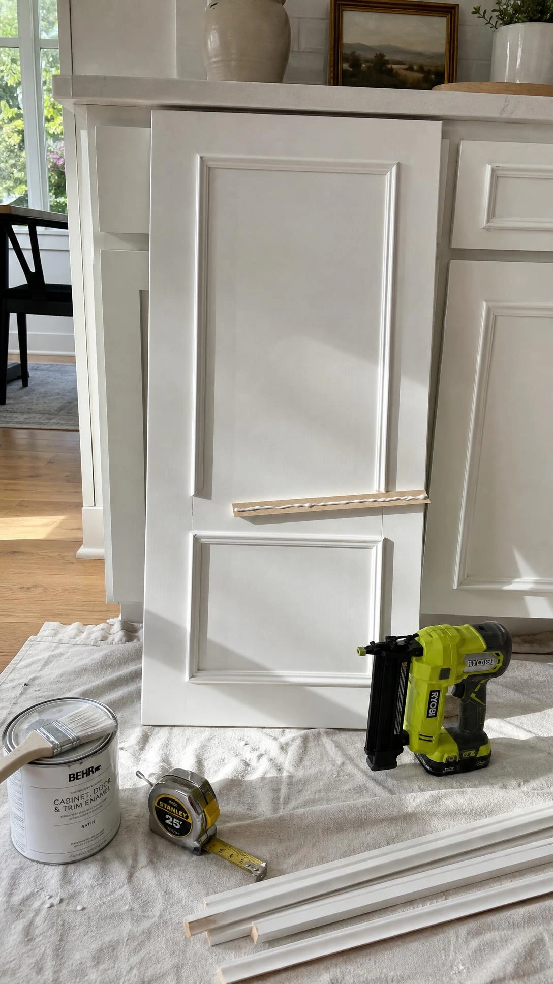 Flat white cabinet door with MDF trim molding pieces arranged in a classic rectangular frame pattern, showing the DIY upgrade in progress