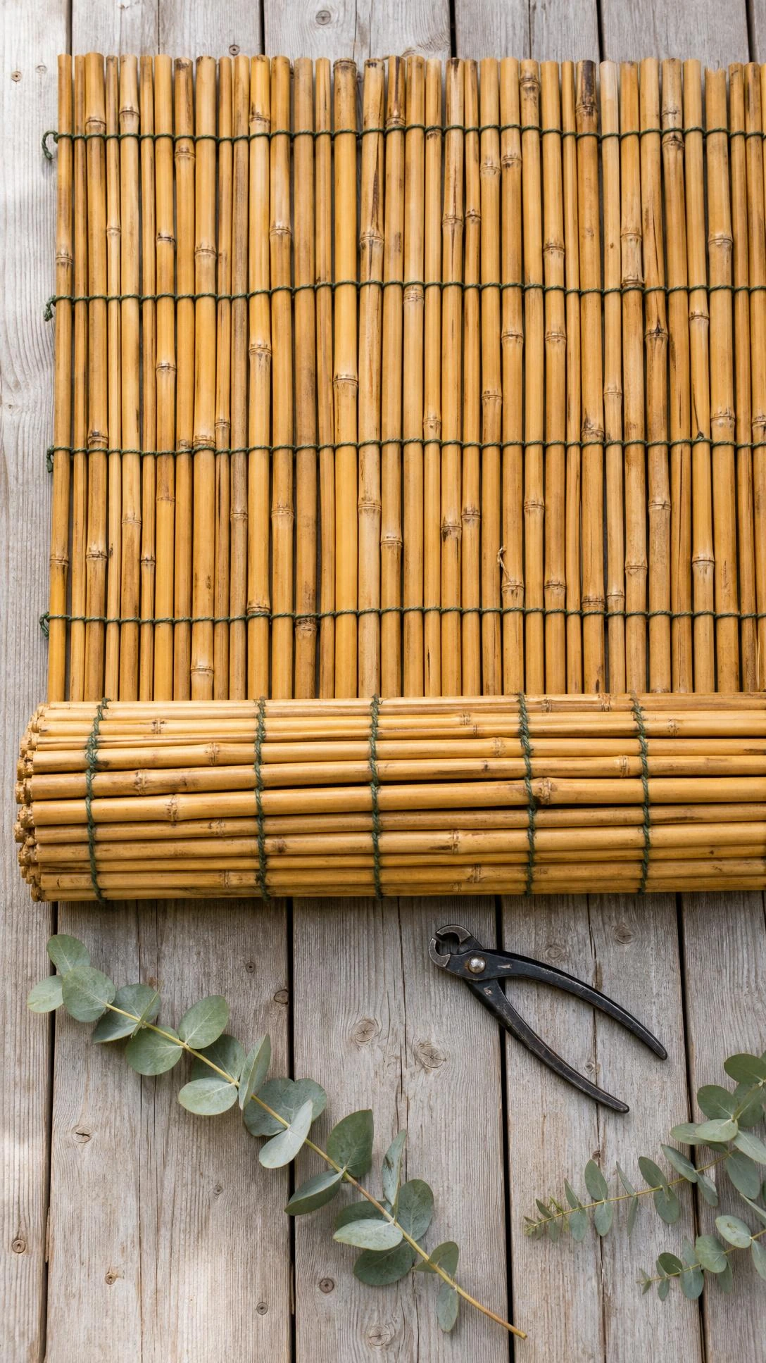 Tightly rolled bamboo fencing panel laid flat on a wooden deck, showing golden-tan canes bound with dark green twine for patio privacy screening