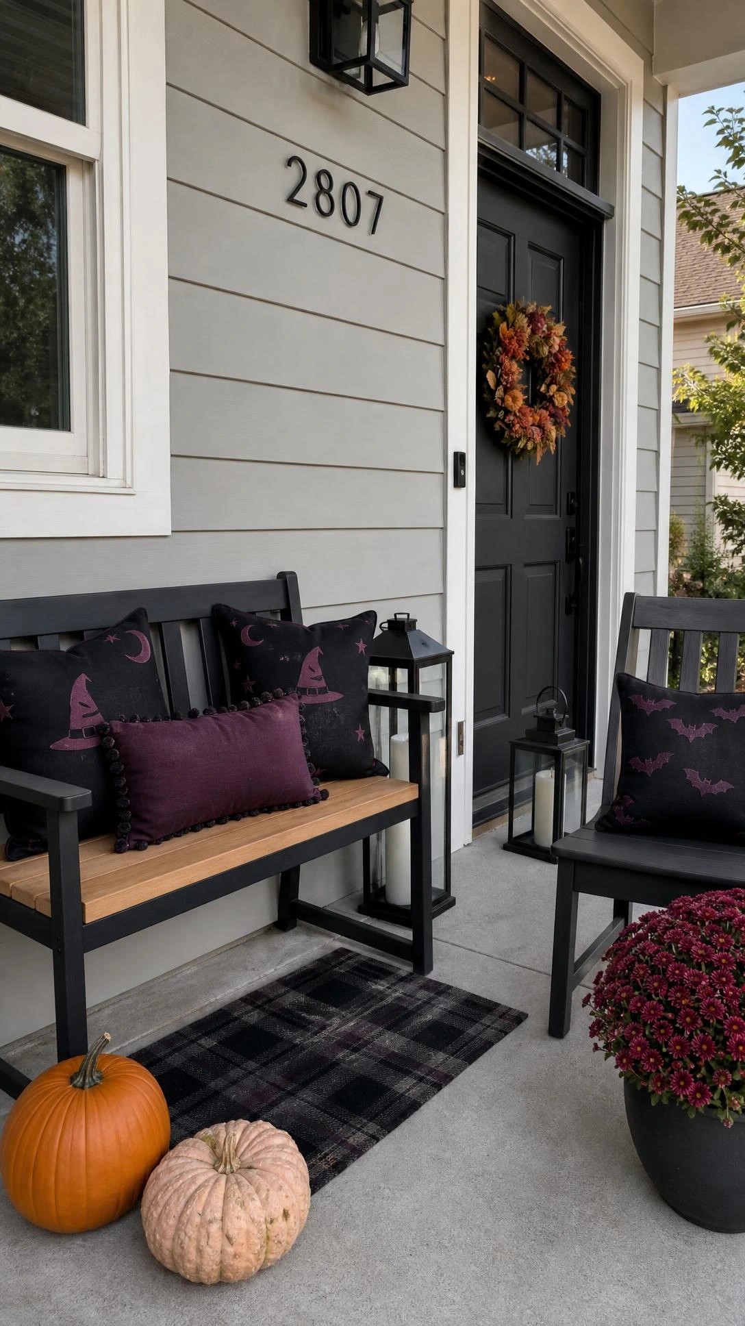 Black and plum Halloween home decor porch pillows style a small painted bench and matching chair, adding moody color to a suburban entry.