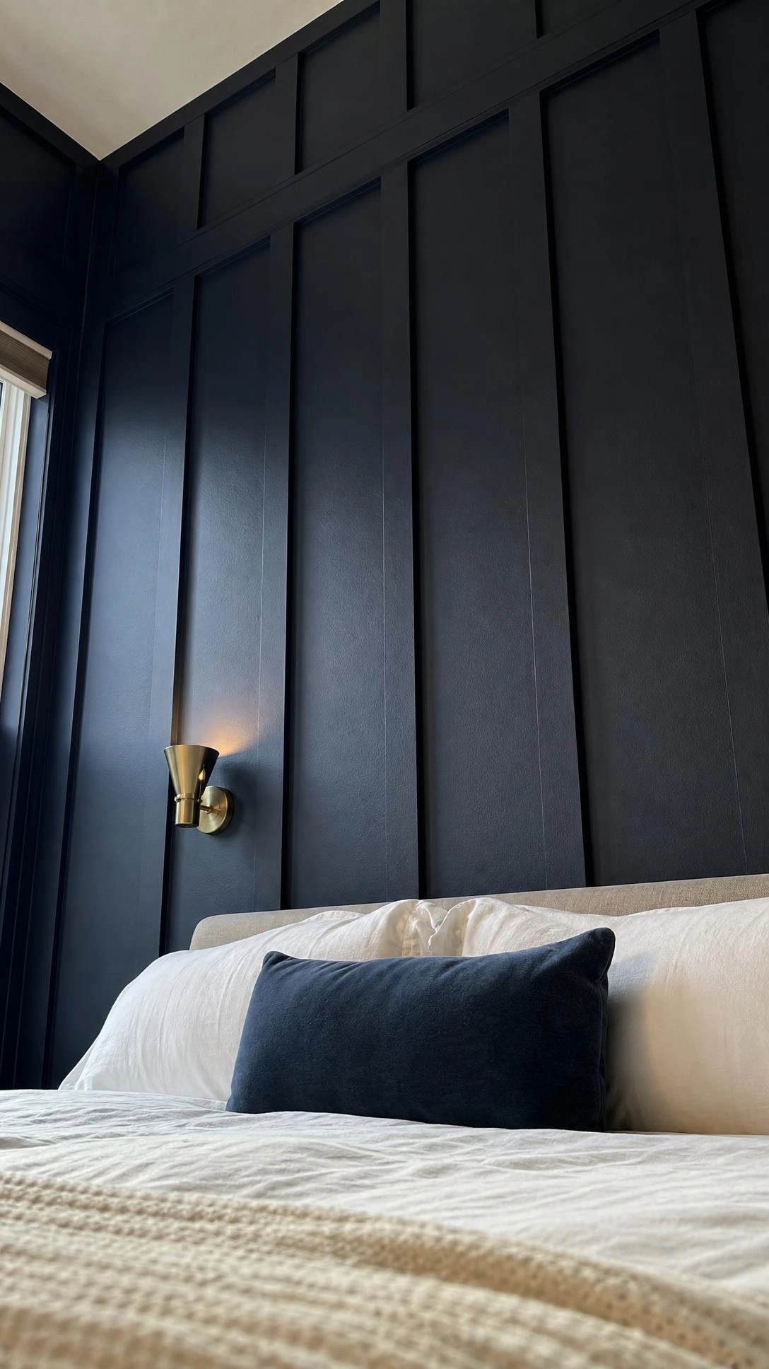 Floor-to-ceiling board and batten panelling painted deep navy blue, with warm raking light casting dramatic vertical shadow lines across a bedroom feature wall