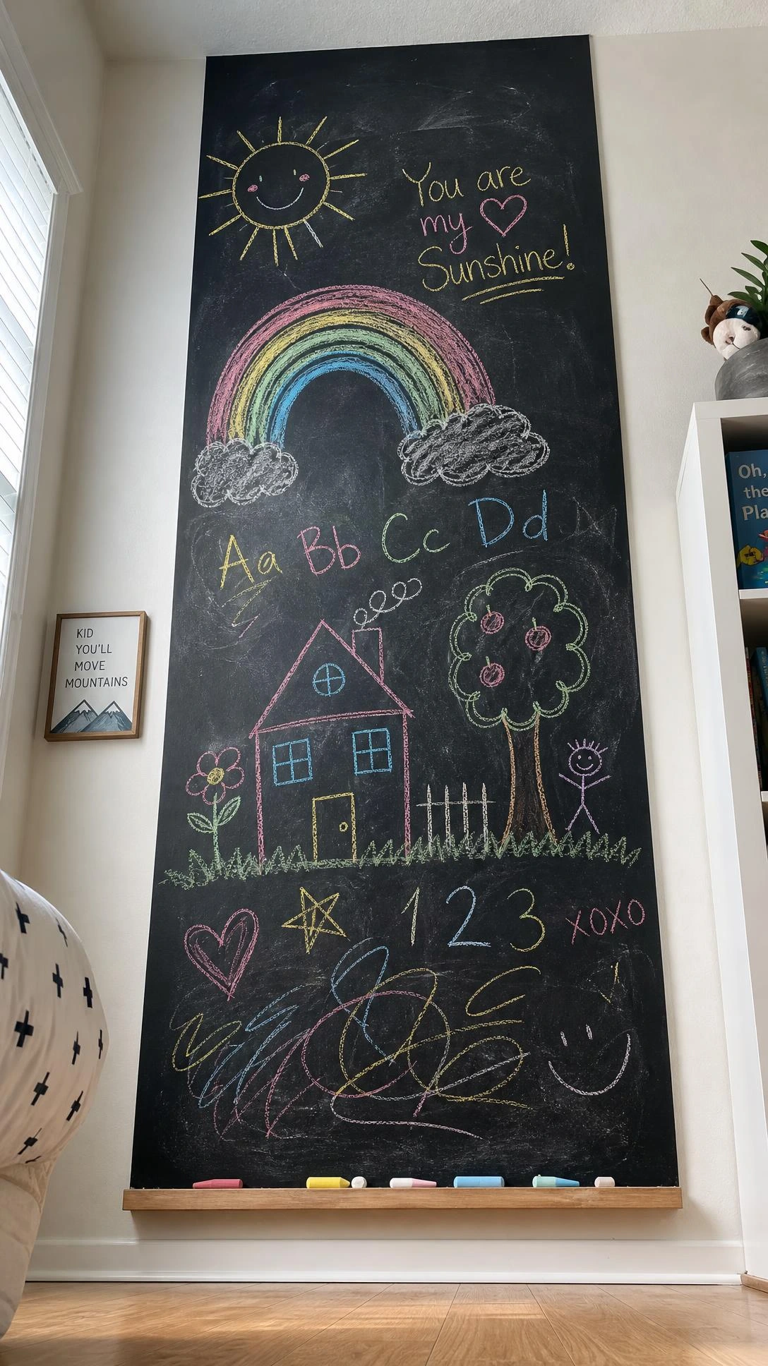 Tall chalkboard paint panel on a child's bedroom wall covered in colorful chalk drawings including a rainbow, sun, and house — a nearly free kids room artwork idea