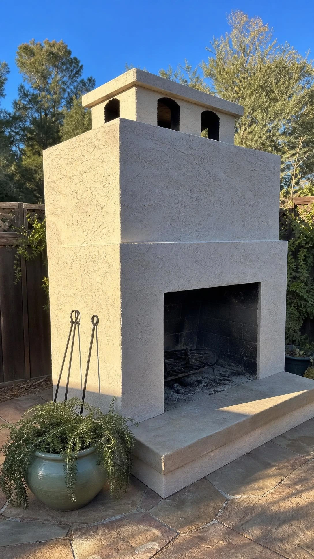 DIY cinder block outdoor fireplace with smooth sandy-white stucco finish photographed from above in a real backyard on a bright afternoon