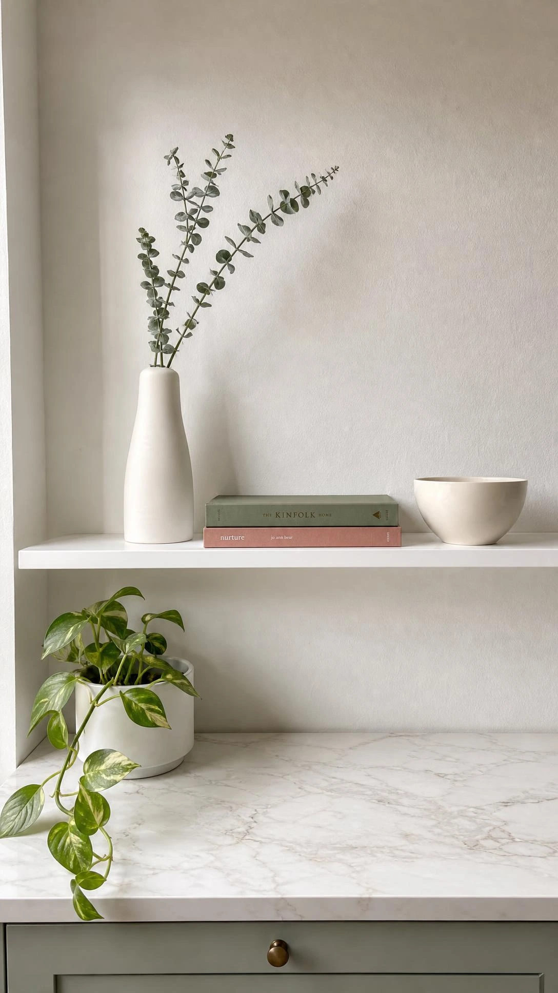 Minimalist kitchen shelf styled with intentional negative space, featuring curated objects on white-painted floating wood against a warm white wall