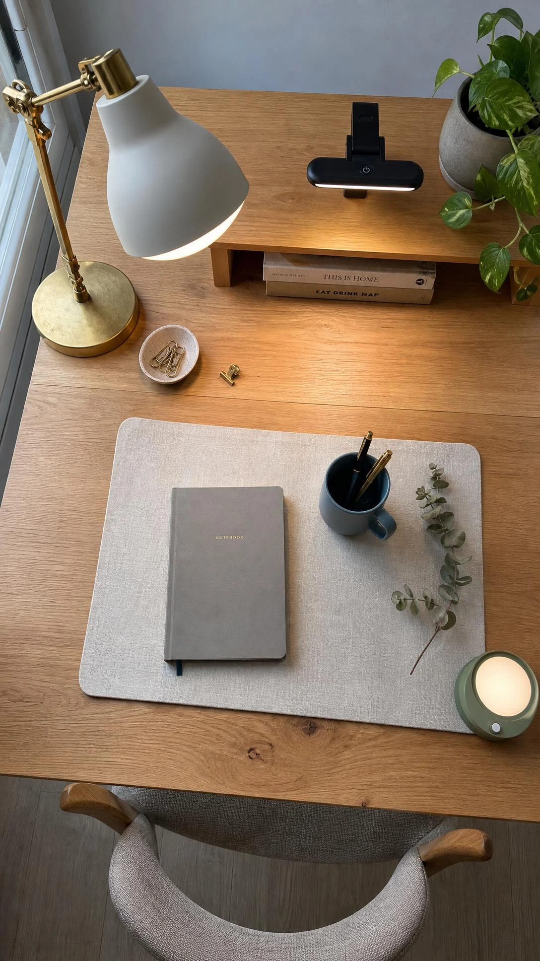 Warm brass desk lamp casting a soft glow across a compact work-from-home desk surface, paired with a matte black clip-on LED light for layered dedicated lighting