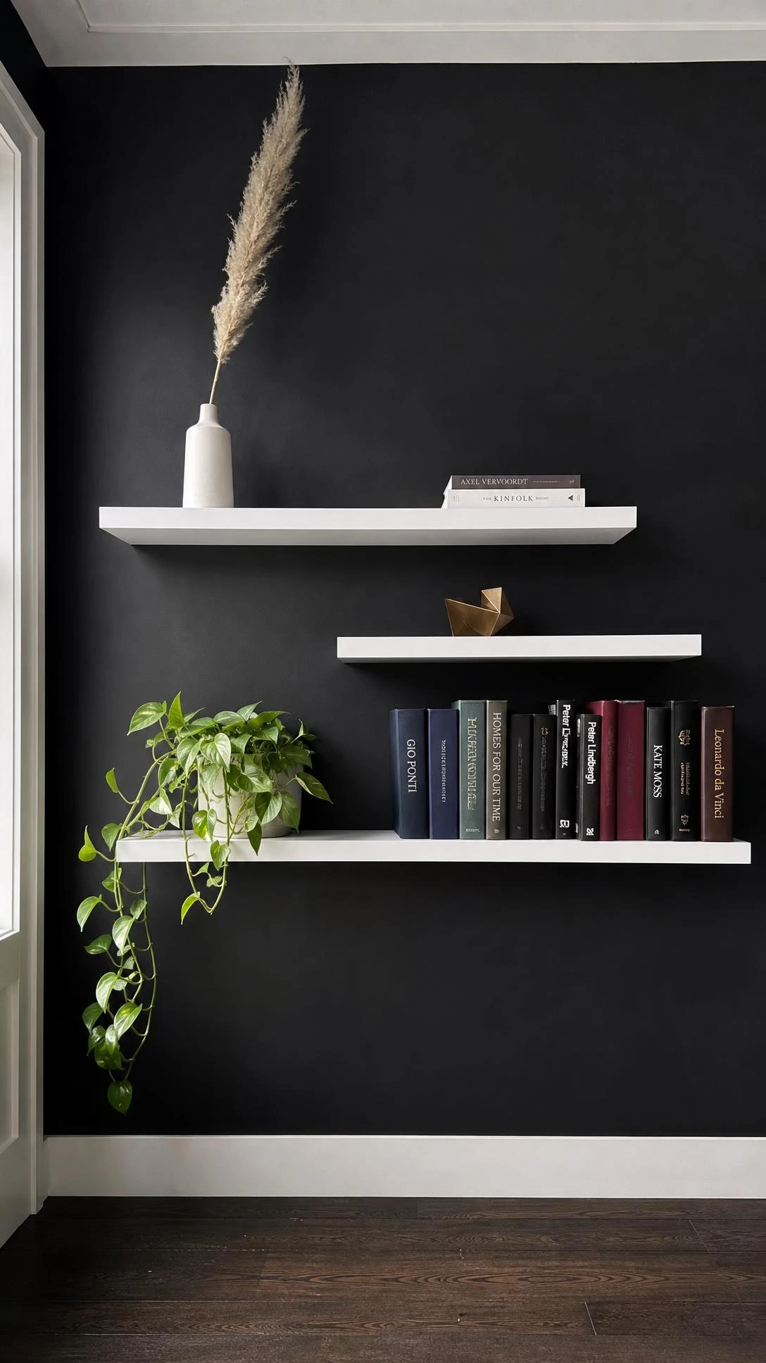 Charcoal-black matte feature wall with staggered white floating shelves built in, creating a dramatic contrast that defines the room
