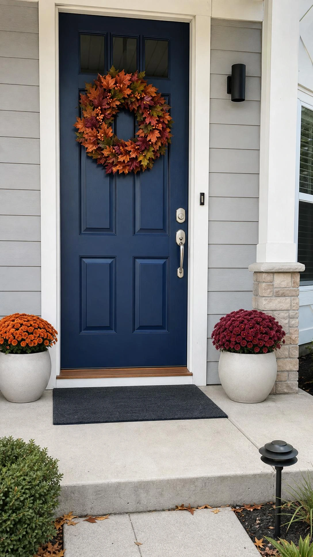 Fall porch decorating ideas start with a layered autumn wreath on a deep navy front door, with burnt orange, burgundy, olive leaves, and berry accents.