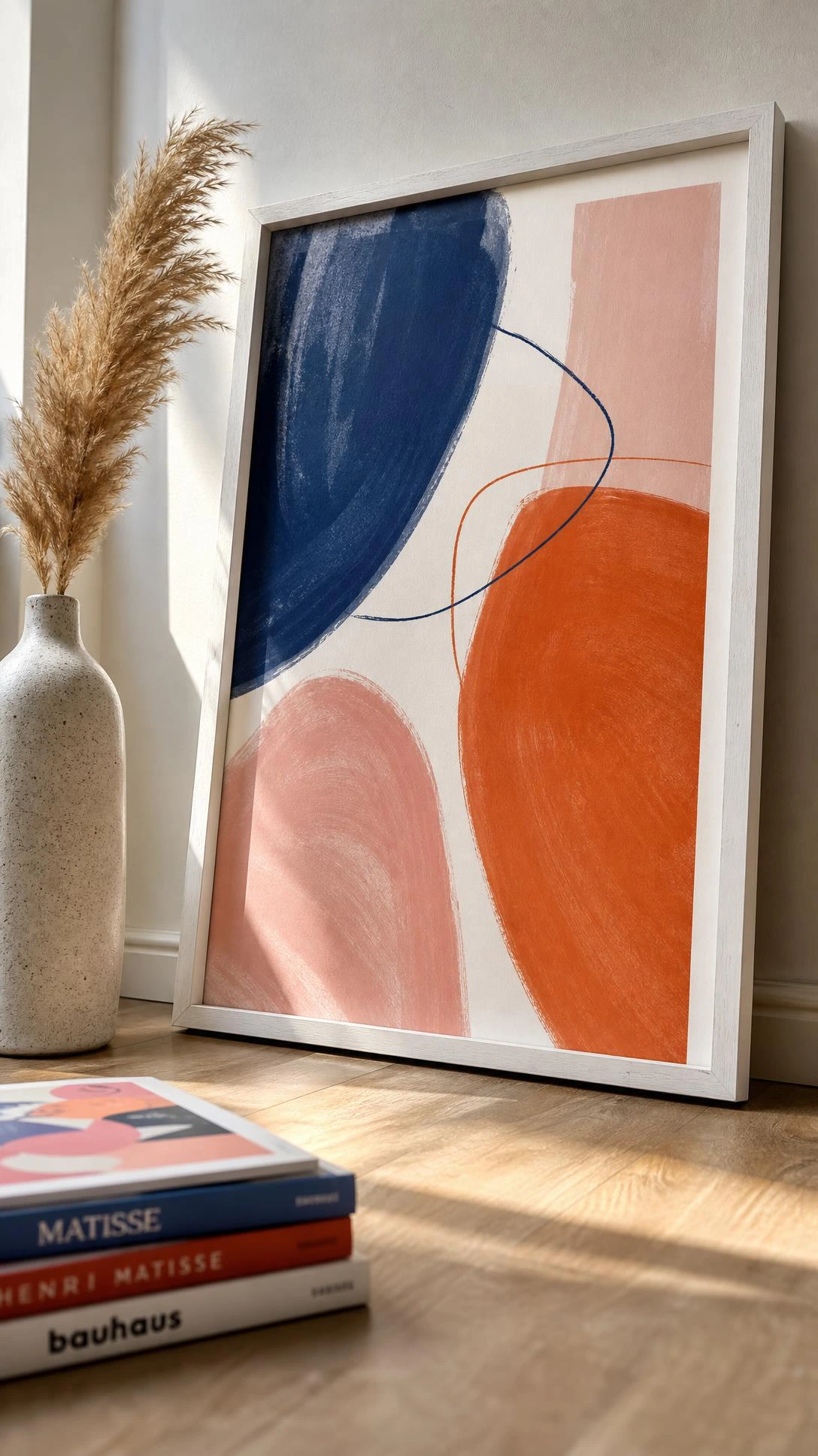 Thin white wood frame leaning against a wall displays a bold cobalt, terracotta, and blush abstract digital art print — free design, zero cost