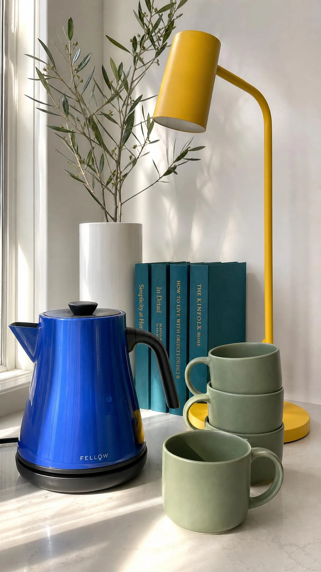 Cobalt blue electric kettle on a white countertop in a bright minimalist living space, showing how colorful functional items add vibrancy without clutter