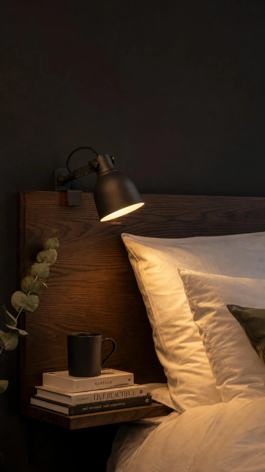 IKEA HEKTAR dark gray spotlight mounted on walnut headboard, casting a warm focused beam over a neatly made bed for a moody bedroom reading setup