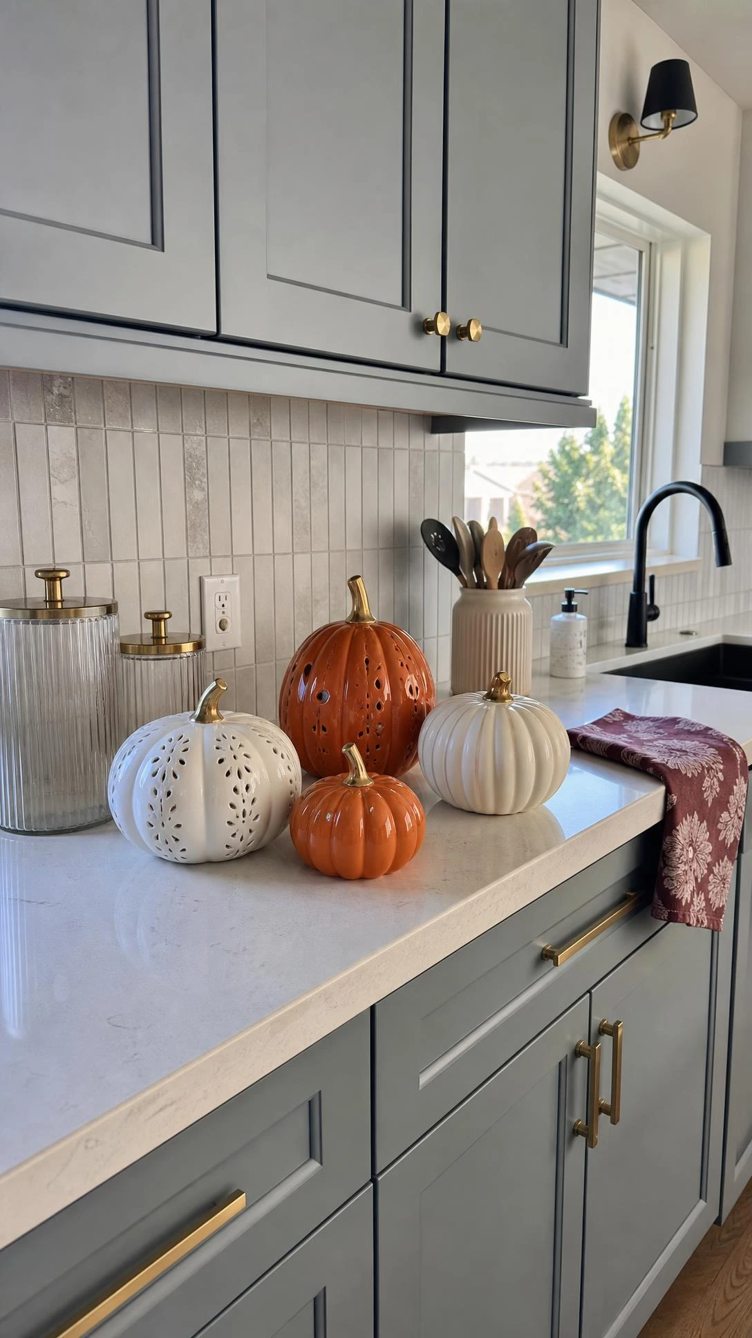 Ceramic pumpkins grouped on a quartz kitchen counter add polished Halloween home decor beside a modern backsplash and gray-blue shaker cabinets.