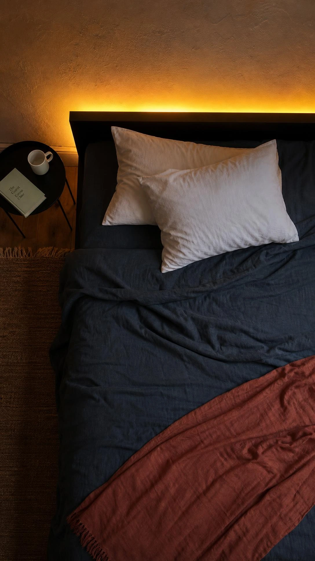 Warm amber LED strip lights glowing behind a low-profile IKEA bed frame, casting a soft golden halo along the bedroom wall for an elevated look