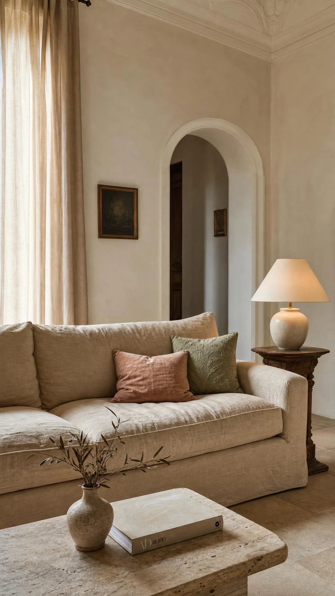 Oat-toned linen sofa anchoring a softly lit Italian living room with tall linen curtains and warm natural daylight