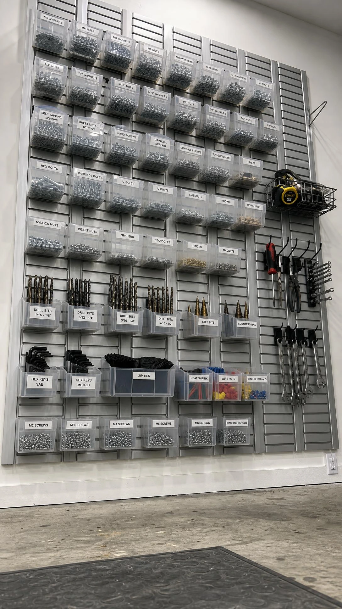Wall-mounted louvered rail system on white garage wall, shot from floor level to show vertical aluminum slats stretching full height for small parts storage