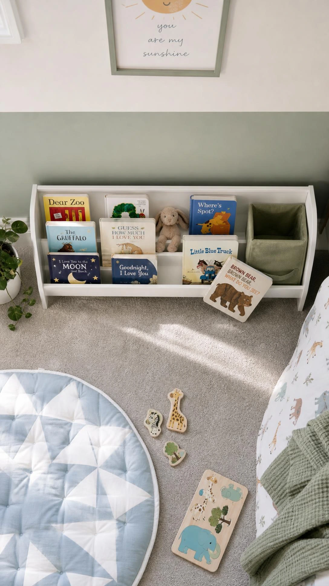 Low front-facing wooden bookshelf in a small toddler bedroom corner displaying colorful board books with visible covers and a tucked plush toy, maximizing floor-level storage