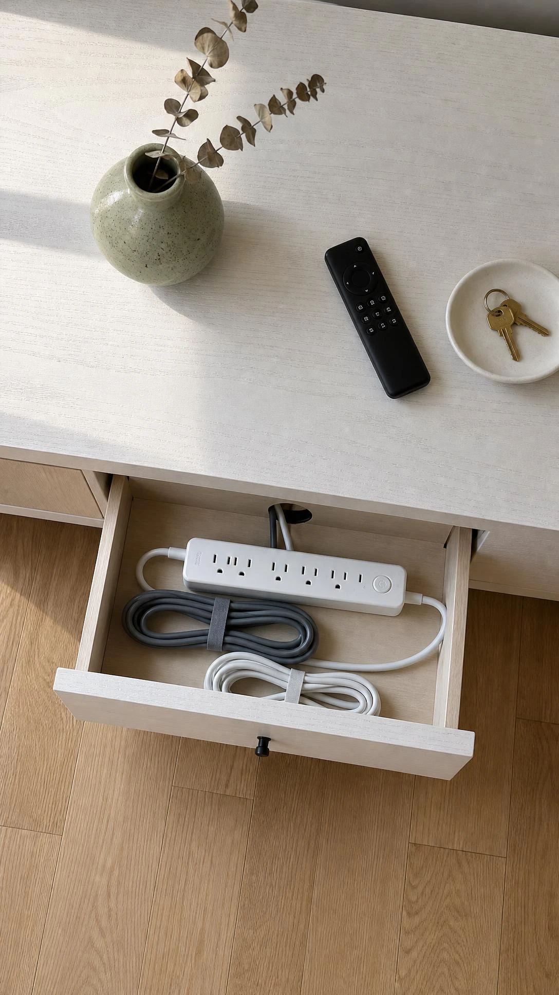 Overhead flat lay of a low-profile wooden TV credenza with pull-out drawer open, revealing a neatly hidden power strip and coiled cables — a clean cable management solution
