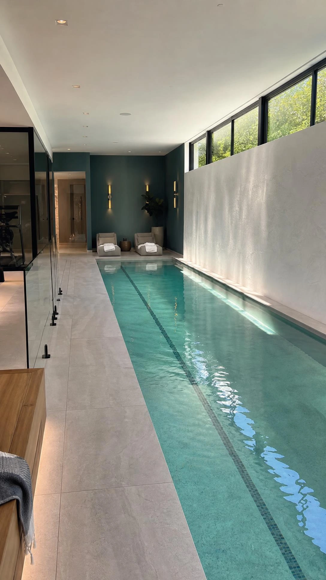 Indoor swimming pool design luxury in a high-end home, with a long narrow lap pool, pale aqua water, porcelain tile, and warm plaster walls.