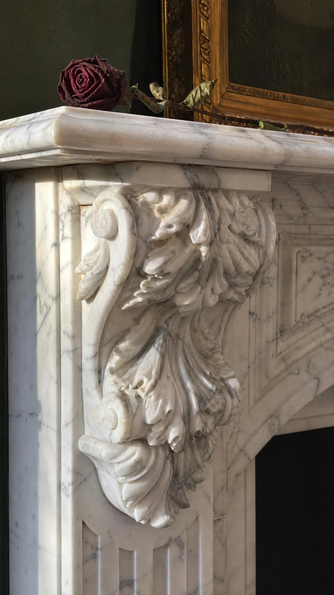 Creamy Carrara marble corbel on a Victorian fireplace mantel, deeply carved acanthus leaf scrollwork casting dramatic shadow relief in warm afternoon window light