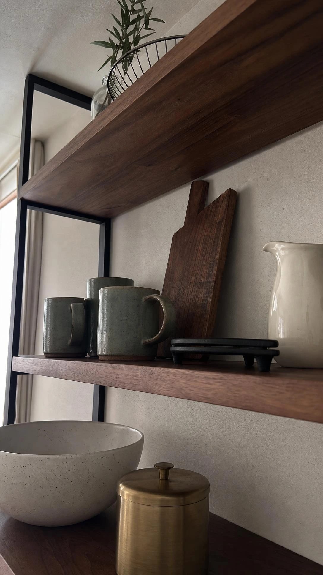 Low-angle view of styled kitchen open shelves mixing warm wood cutting boards, ceramic bowls, and metal accents for a layered, curated look
