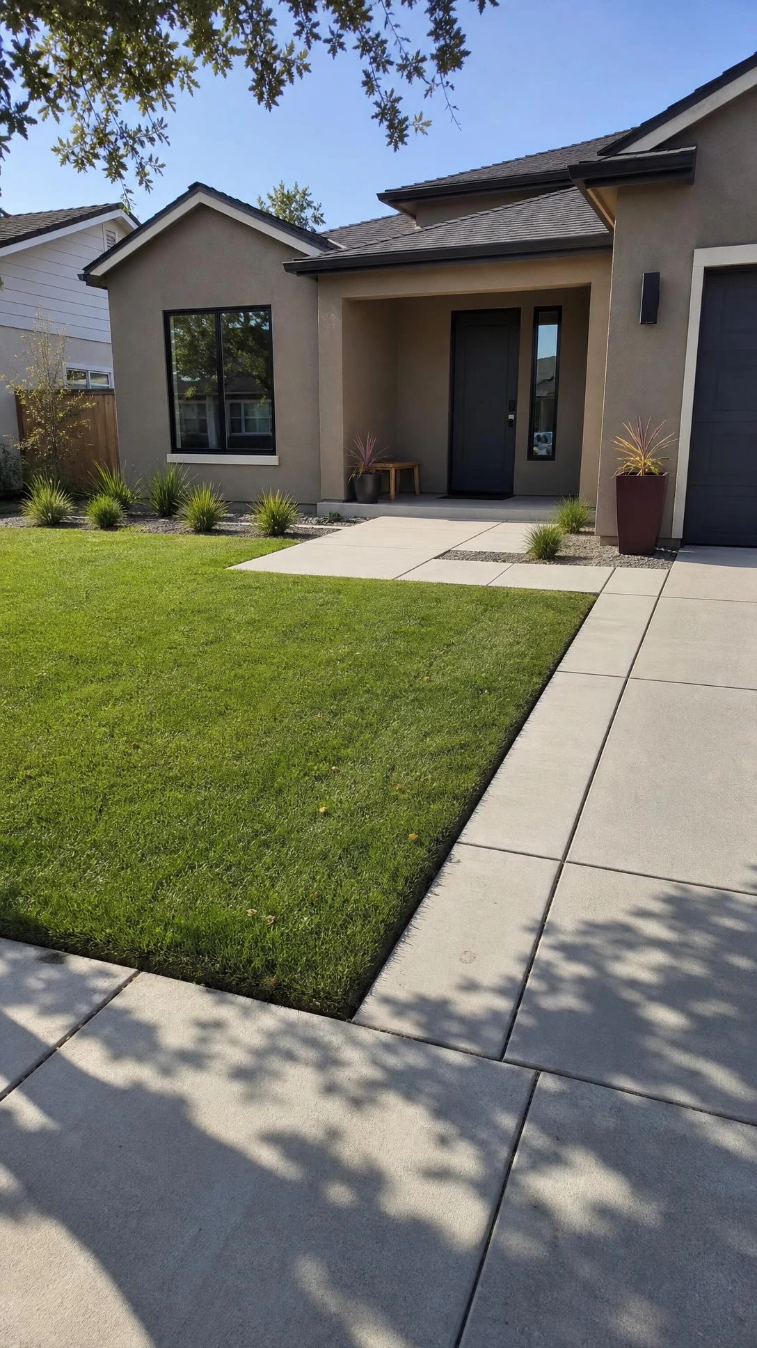 Modern Landscape Design with a rectangular green front lawn, poured-concrete walkways and driveway bands framing a taupe stucco home.