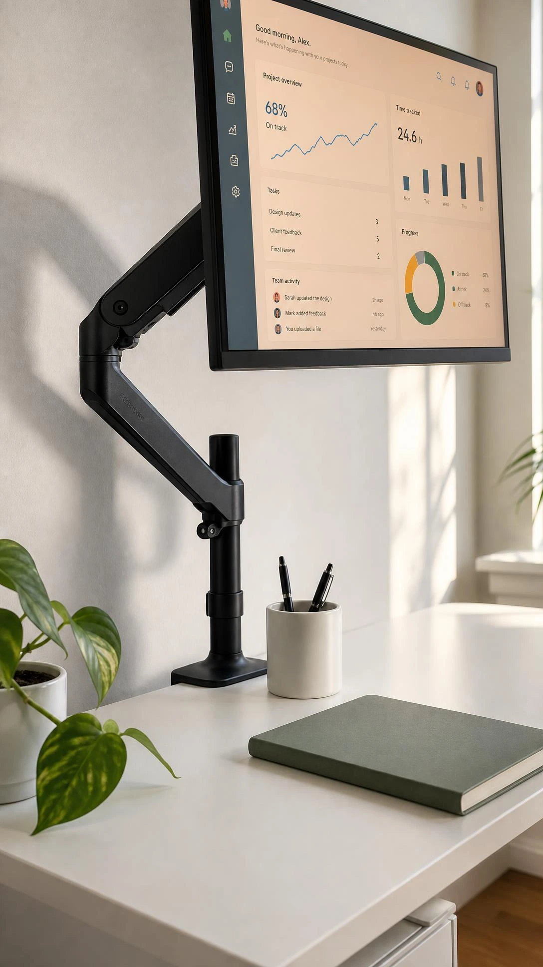Matte black monitor arm mounted to a compact white desk, lifting a slim 24-inch monitor to eye level with cables neatly routed through the arm's built-in channel