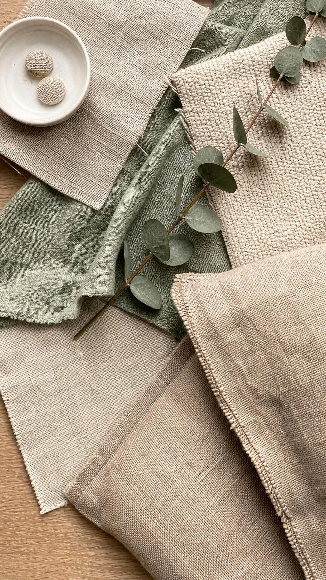 Overhead flat lay of linen, boucle, and cotton muslin swatches on light oak — natural fabric upholstery options for a chic living room