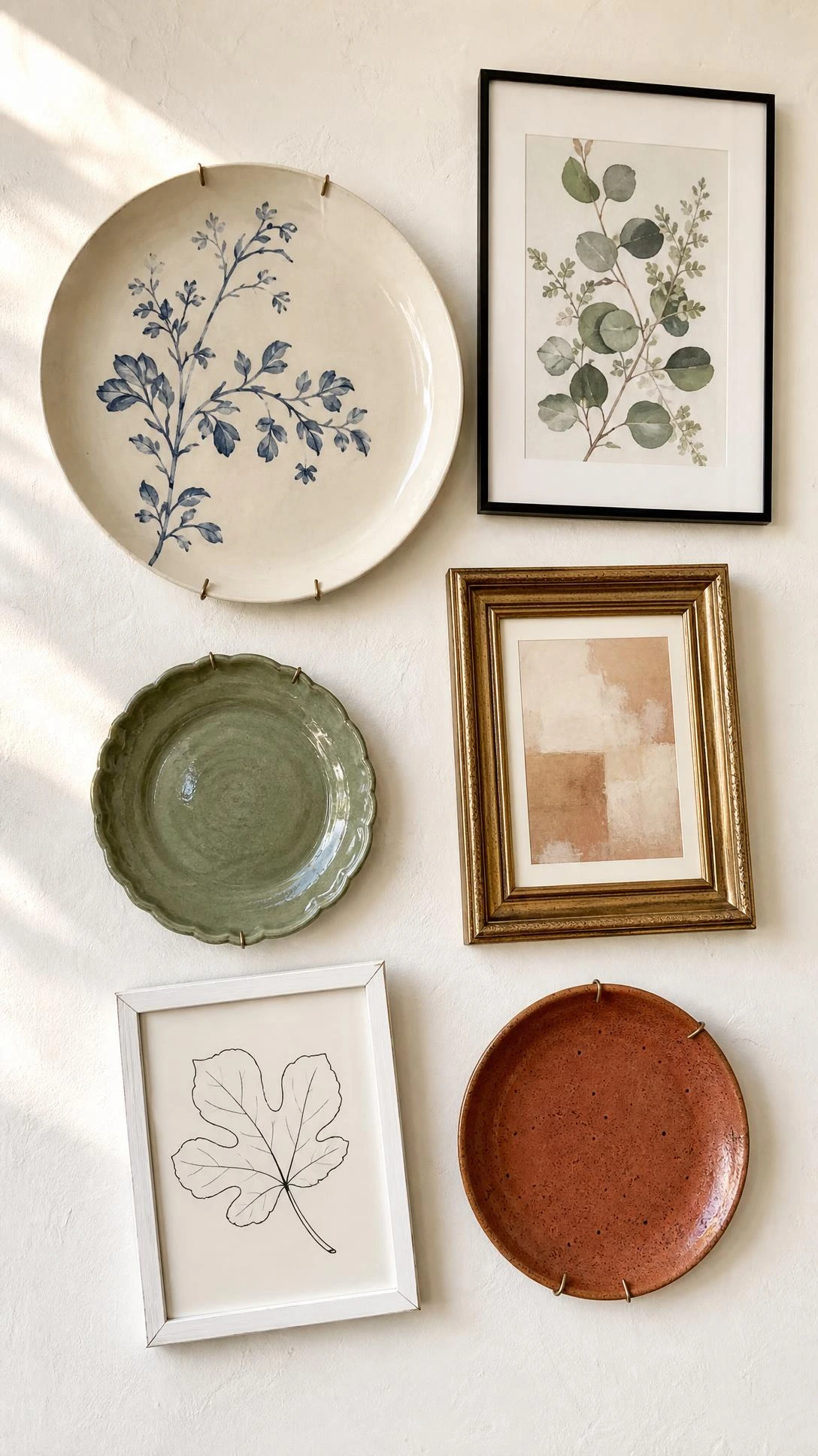 Flat lay of dining room gallery wall layout combining decorative plates and framed art on warm white surface for pre-hanging arrangement planning
