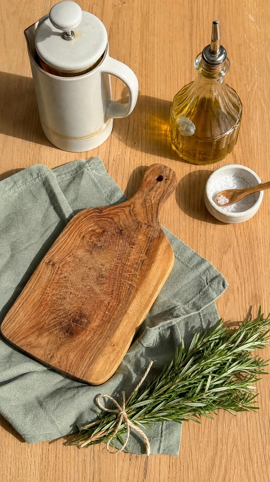 Overhead flat lay of a light oak kitchen shelf with a matte white ceramic French press and olive wood cutting board showing real daily use marks — practical kitchen shelves decor that earns its space