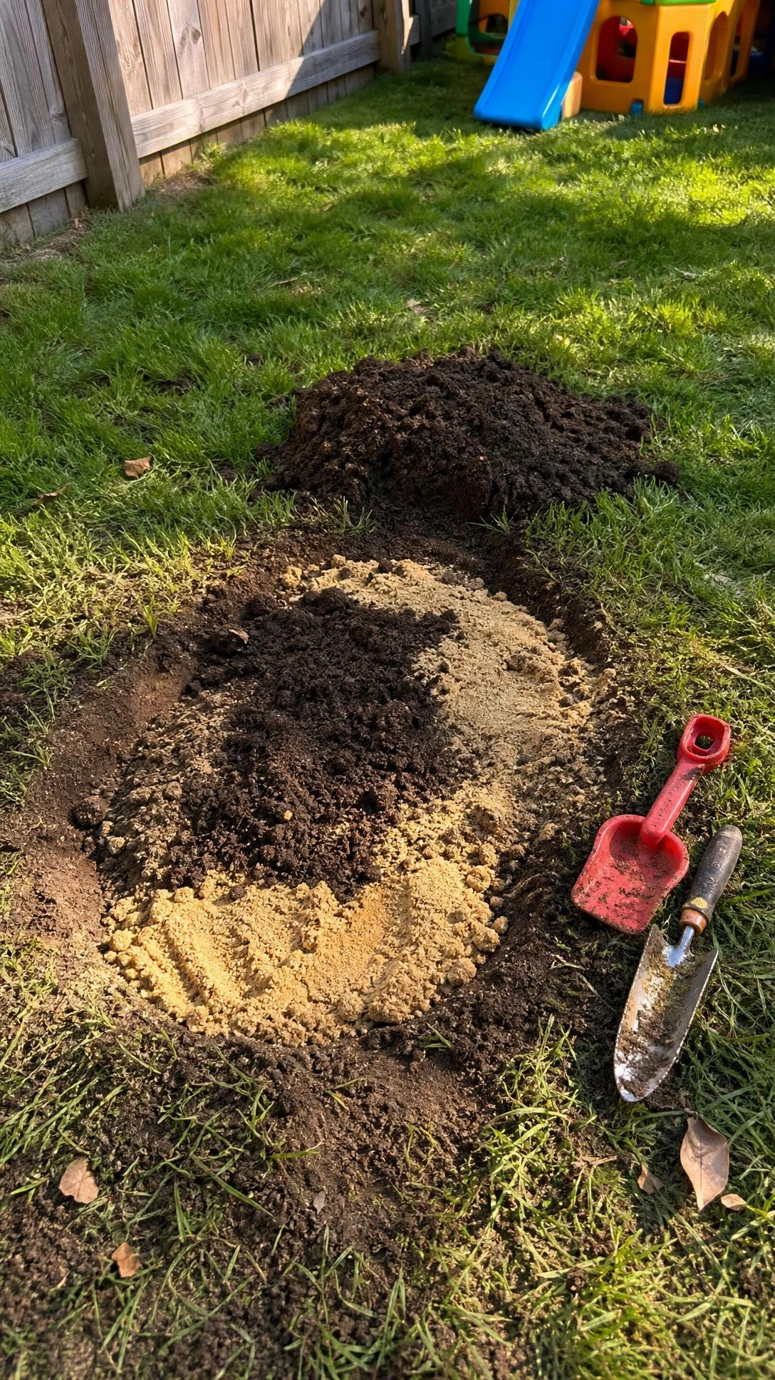 A sunken lawn depression being filled with topsoil and sand mix in a family backyard, showing the simple leveling fix kids can help with