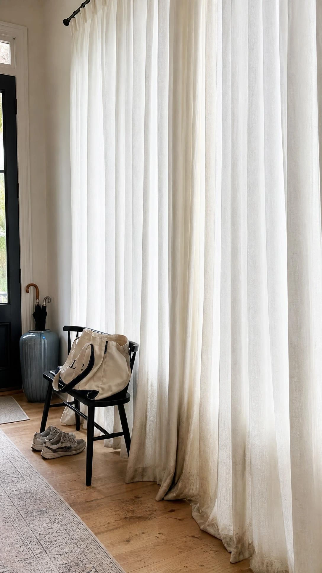 Floor-to-ceiling sheer white curtains hanging in a high-traffic entryway, visibly yellowed and dingy along the lower hem — a common curtain color mistake in busy living spaces