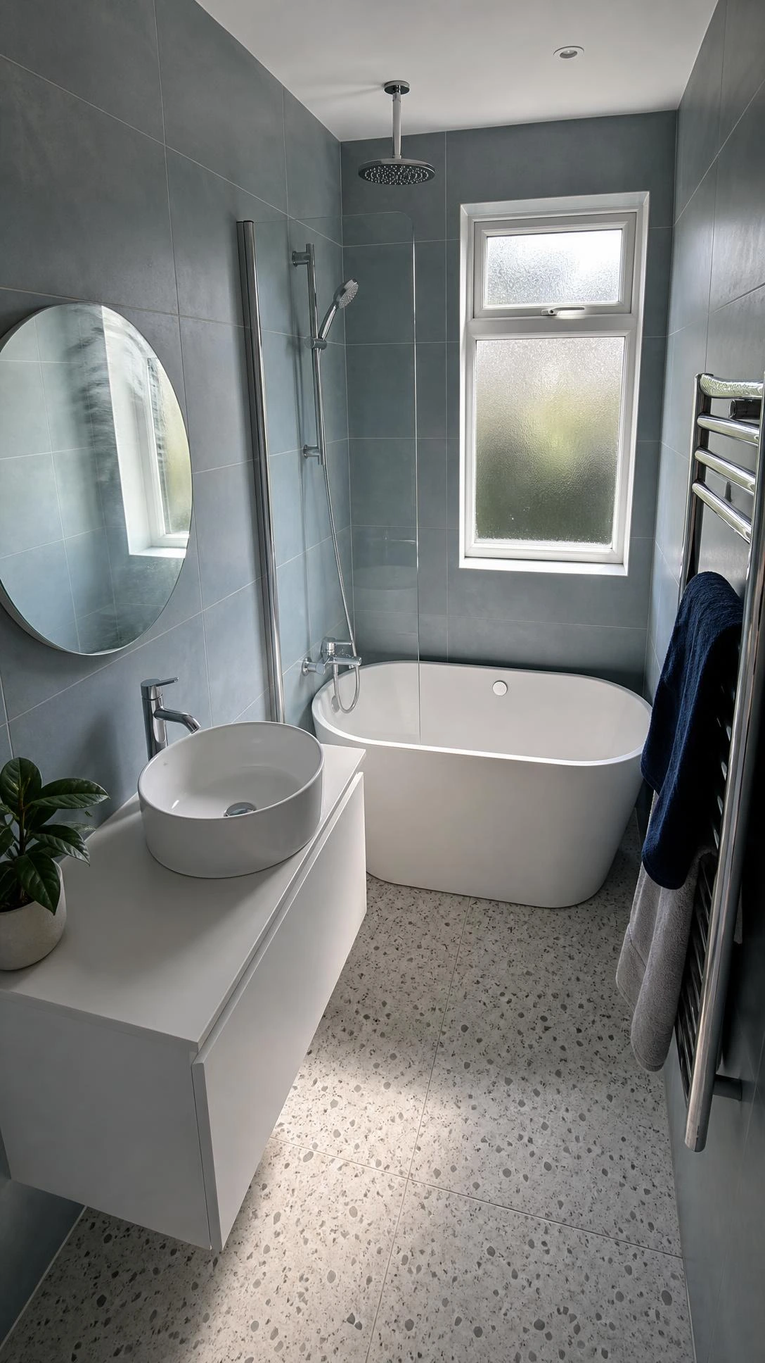 Compact family bathroom with freestanding white bath, fixed glass shower screen, and brushed chrome ceiling rainfall showerhead maximising a small floor plan