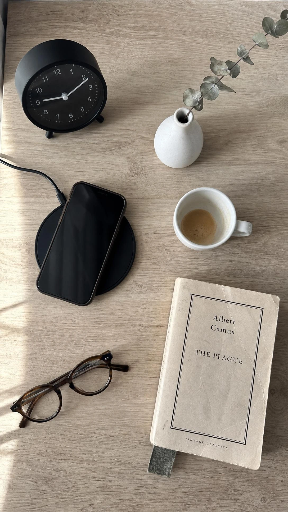 Overhead flat lay of a wooden nightstand in a shared kids' room styled with a matte black wireless charger, espresso cup, and ceramic bud vase as a small adult sanctuary