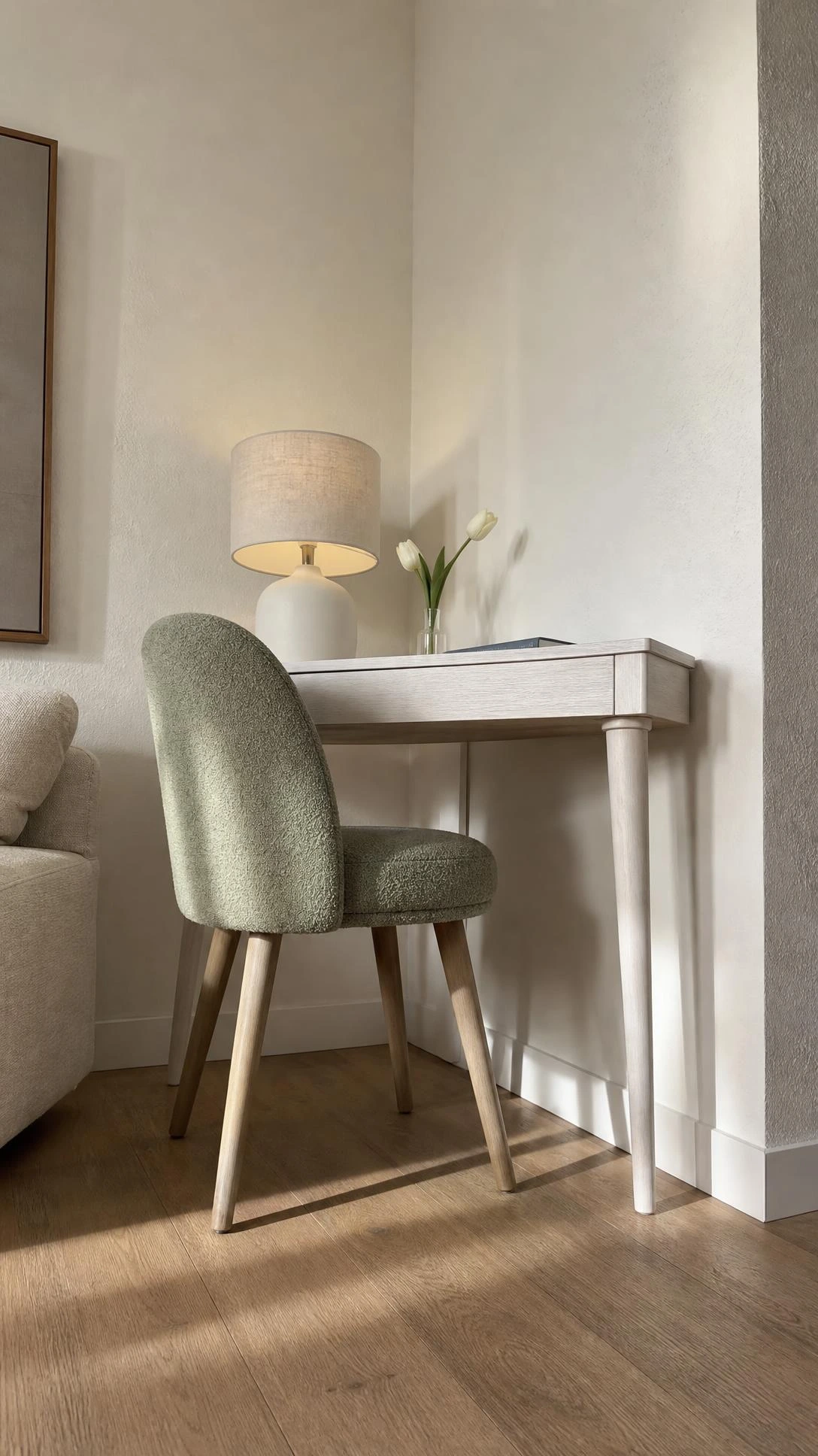 Slim whitewashed writing desk with tapered legs styled as a corner console in a living room, shot from floor level to highlight the architectural corner above